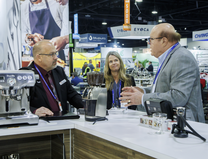 Exhibitor speaks to two show participants behind coffee brewing equipment